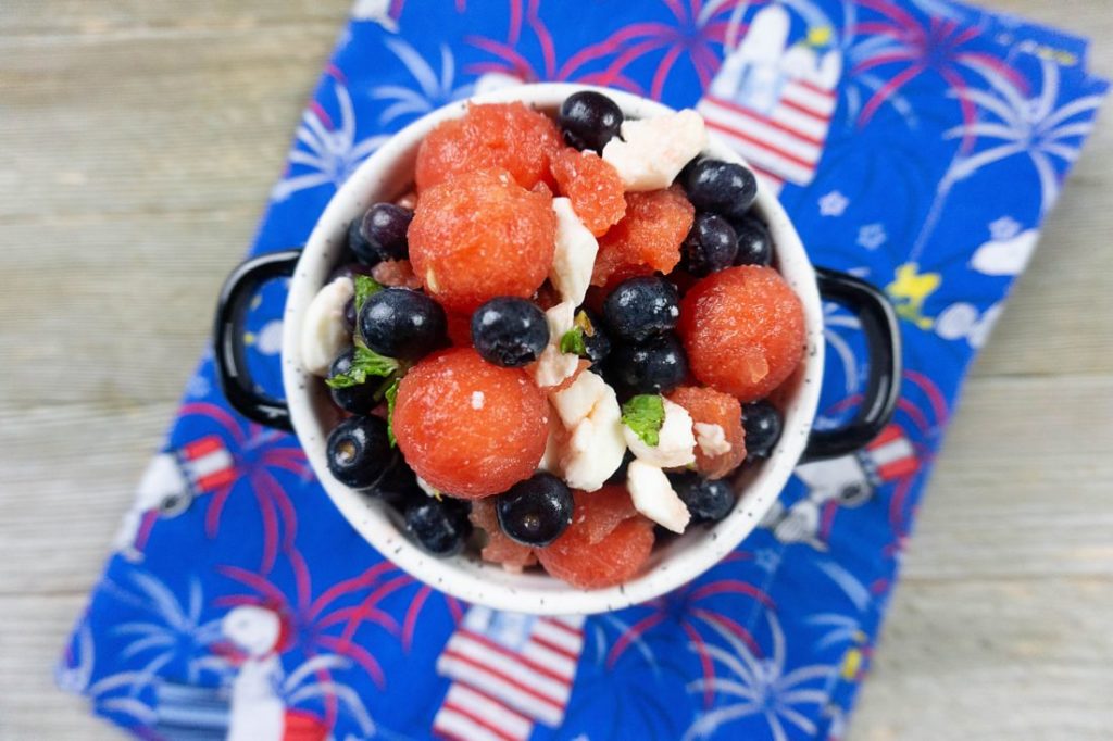 Watermelon, pearl mozzarella, blueberries, and mint in a white bowl on a snoopy cloth napkin