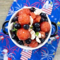 Watermelon, pearl mozzarella, blueberries, and mint in a white bowl on a snoopy cloth napkin