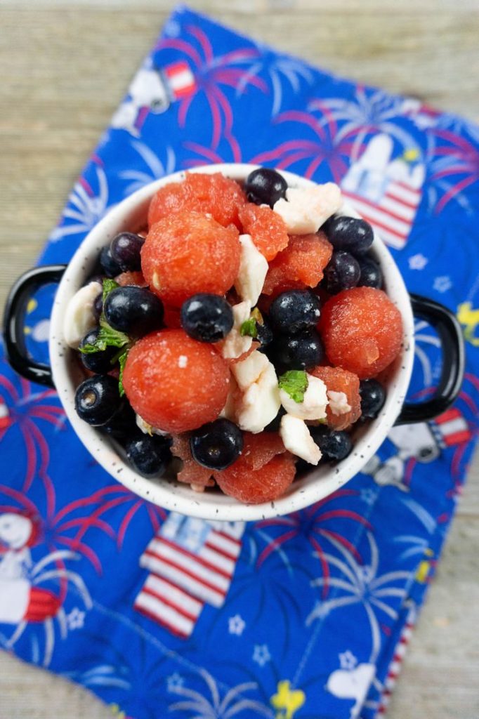 Watermelon, pearl mozzarella, blueberries, and mint in a white bowl on a snoopy cloth napkin