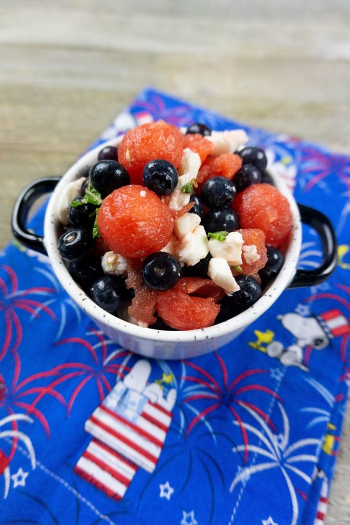 Watermelon, pearl mozzarella, blueberries, and mint in a white bowl on a snoopy cloth napkin