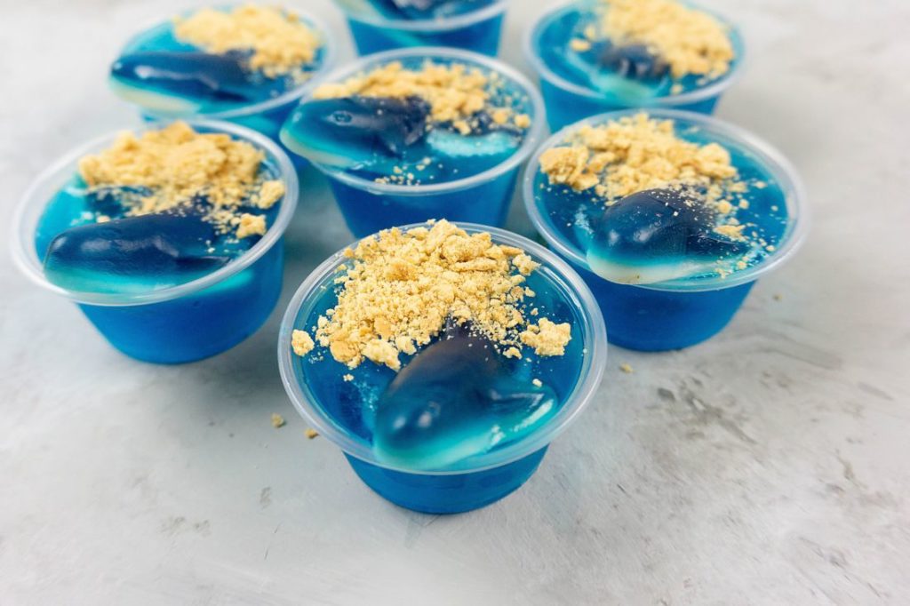 Shark Beach Jello Shots with gummy sharks, graham crackers as sand, and blue jello.