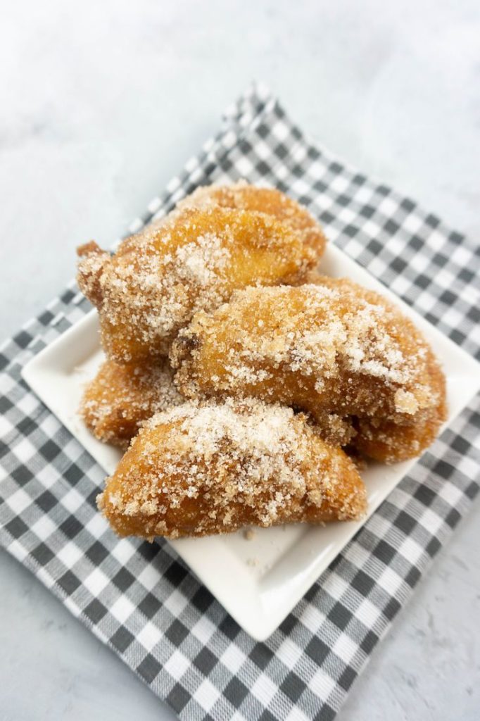 Deep fried apples on a white plate with cinnamon sugar on top on a plaid napkin and concrete backdrop