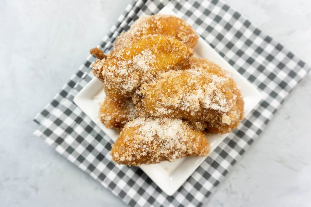 Deep fried apples on a white plate with cinnamon sugar on top on a plaid napkin and concrete backdrop