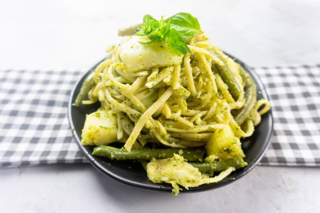 linguine noodles with pesto, potatoes, and green beans on a black plate with concrete backdrop