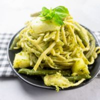 linguine noodles with pesto, potatoes, and green beans on a black plate with concrete backdrop