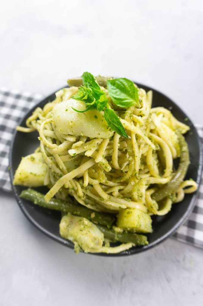 linguine noodles with pesto, potatoes, and green beans on a black plate with concrete backdrop