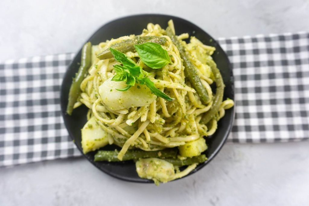 linguine noodles with pesto, potatoes, and green beans on a black plate with concrete backdrop