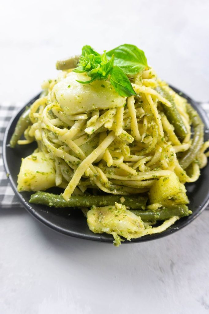 linguine noodles with pesto, potatoes, and green beans on a black plate with concrete backdrop