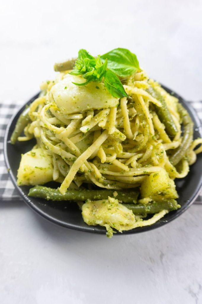 linguine noodles with pesto, potatoes, and green beans on a black plate with concrete backdrop