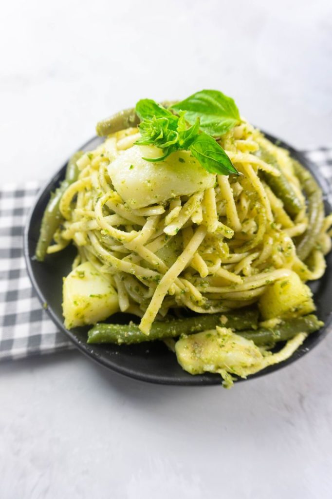 linguine noodles with pesto, potatoes, and green beans on a black plate with concrete backdrop