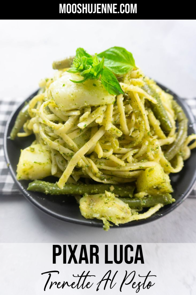 linguine noodles with pesto, potatoes, and green beans on a black plate with concrete backdrop