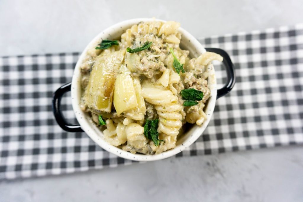 Spinach Artichoke Dip Beef Pasta in a white and black bowl on concrete backdrop