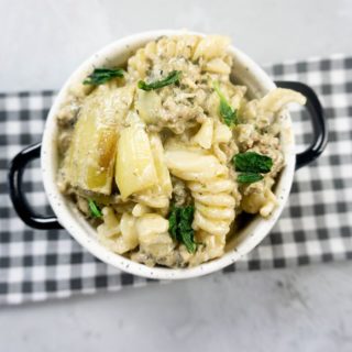 Spinach Artichoke Dip Beef Pasta in a white and black bowl on concrete backdrop