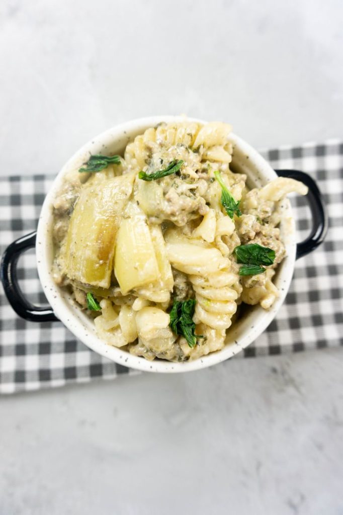 Spinach Artichoke Dip Beef Pasta in a white and black bowl on concrete backdrop