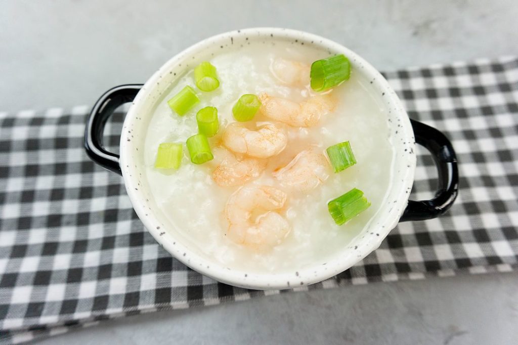 Disney Raya Shrimp Congee in a white bowl with plaid gray napkin on a concrete backdrop