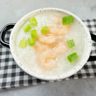 Disney Raya Shrimp Congee in a white bowl with plaid gray napkin on a concrete backdrop