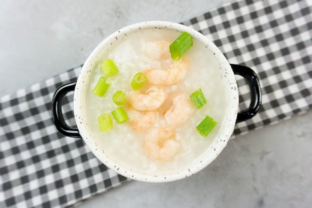 Disney Raya Shrimp Congee in a white bowl with plaid gray napkin on a concrete backdrop