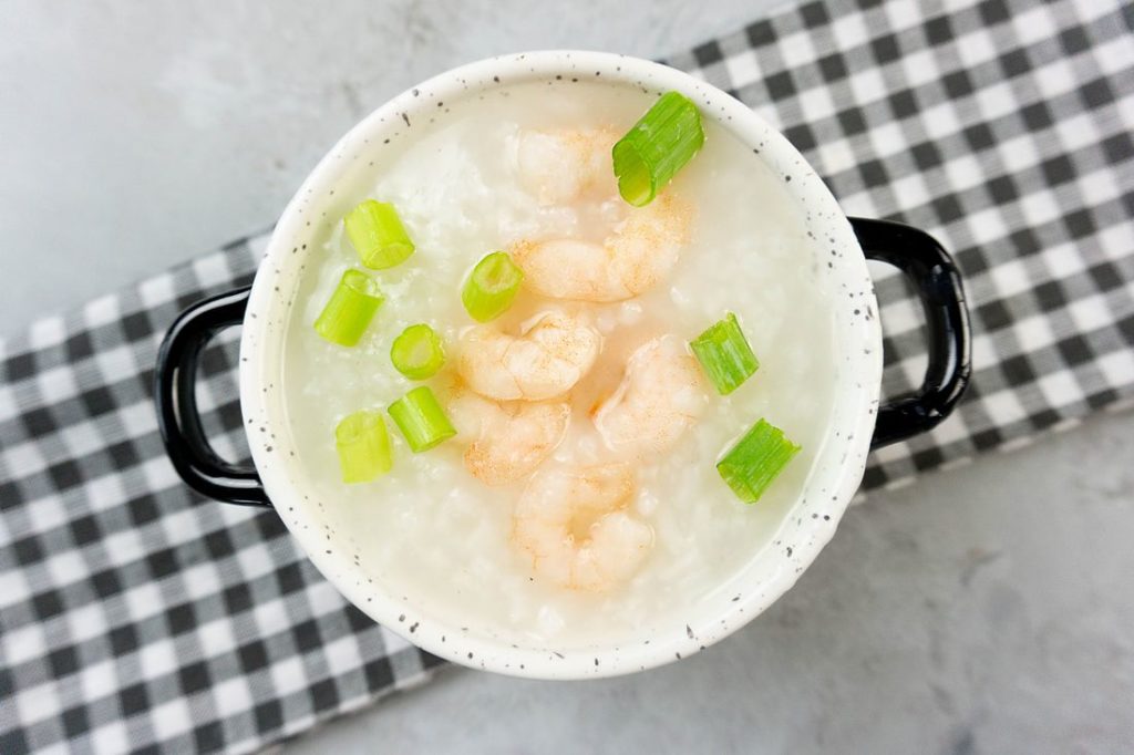 Disney Raya Shrimp Congee in a white bowl with plaid gray napkin on a concrete backdrop