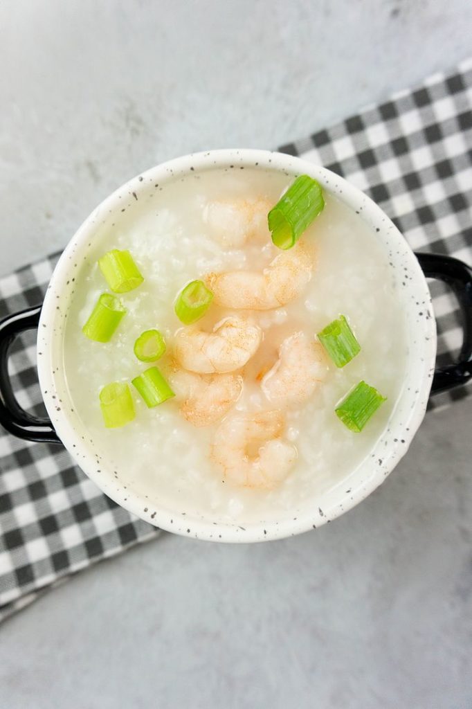 Disney Raya Shrimp Congee in a white bowl with plaid gray napkin on a concrete backdrop