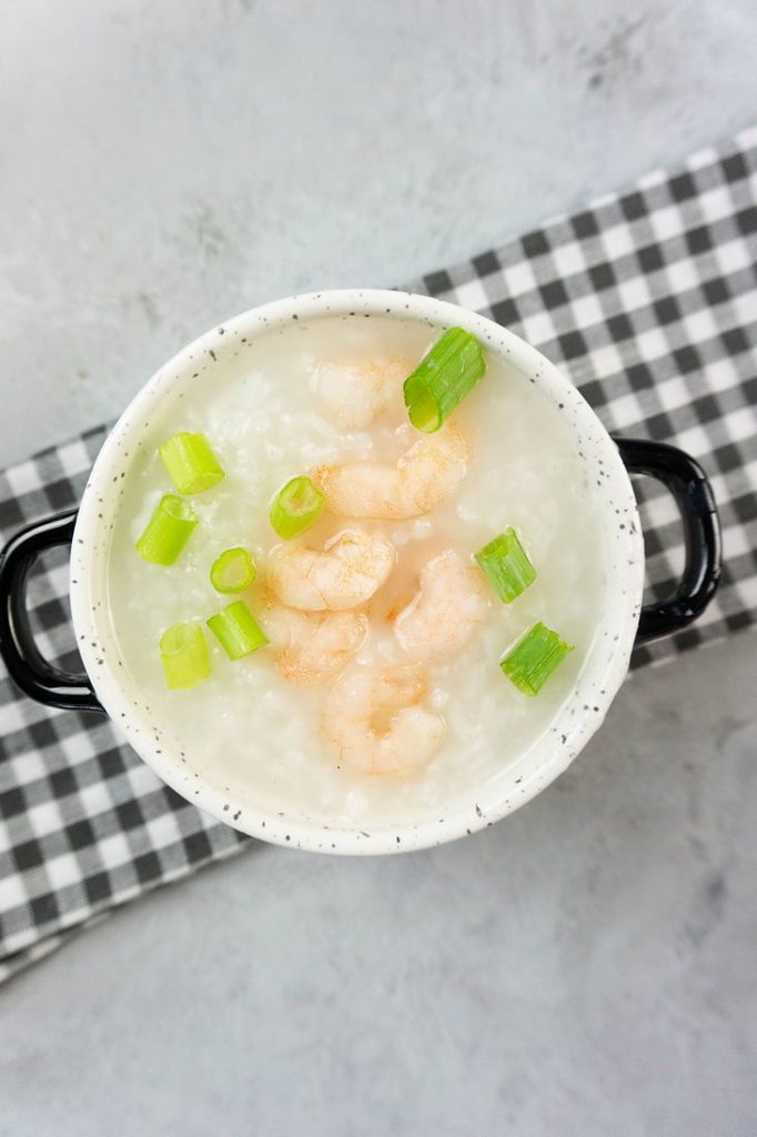 Disney Raya Shrimp Congee in a white bowl with plaid gray napkin on a concrete backdrop