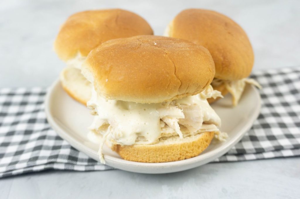 Instant Pot Alabama White Sauce Sliders on a white plate with gray plaid napkin and concrete back drop