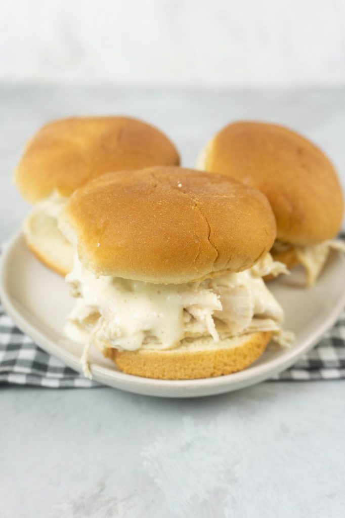 Instant Pot Alabama White Sauce Sliders on a white plate with gray plaid napkin and concrete back drop