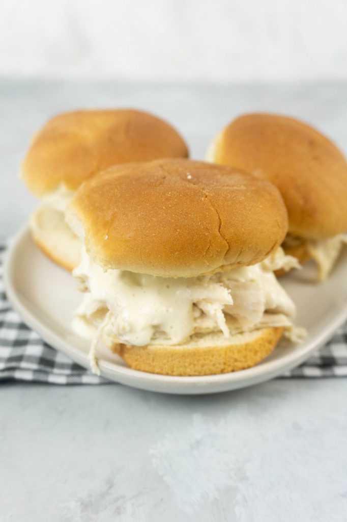 Instant Pot Alabama White Sauce Sliders on a white plate with gray plaid napkin and concrete back drop