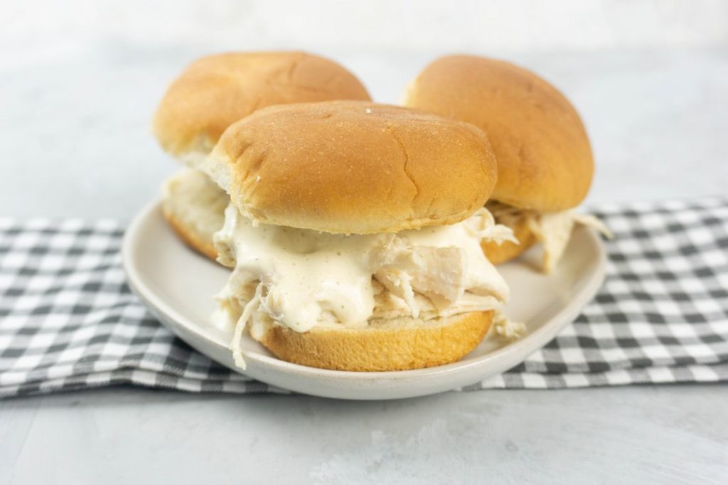 Instant Pot Alabama White Sauce Sliders on a white plate with gray plaid napkin and concrete back drop