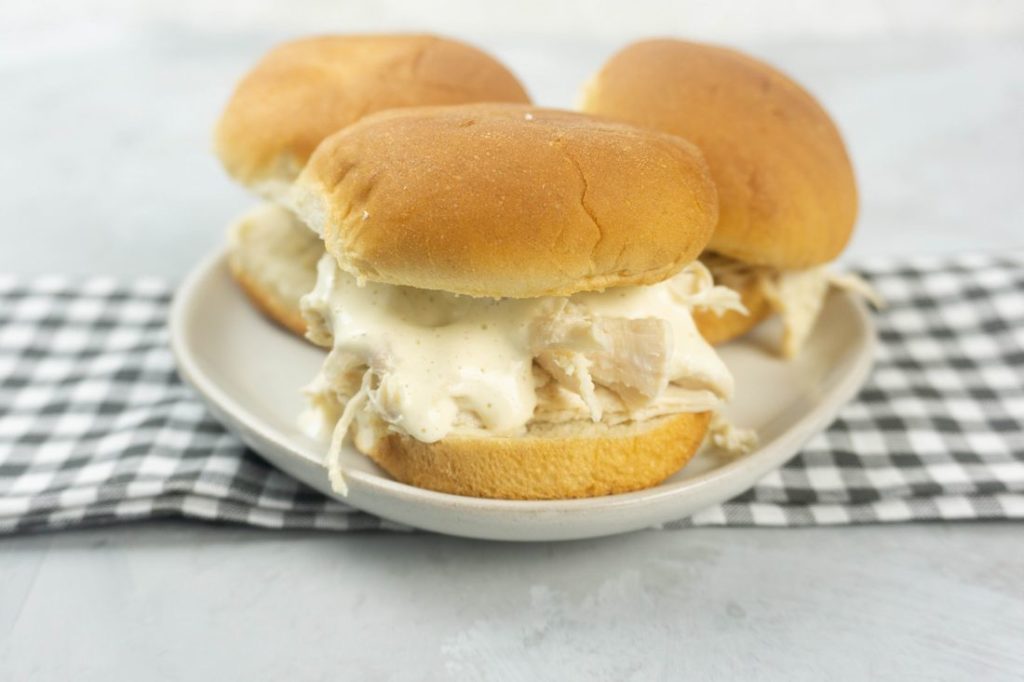 Instant Pot Alabama White Sauce Sliders on a white plate with gray plaid napkin and concrete back drop