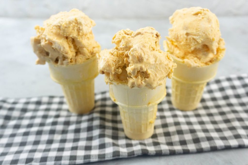 Pumpkin ginger snap ice cream in a cone on a plaid napkin with a concrete backdrop