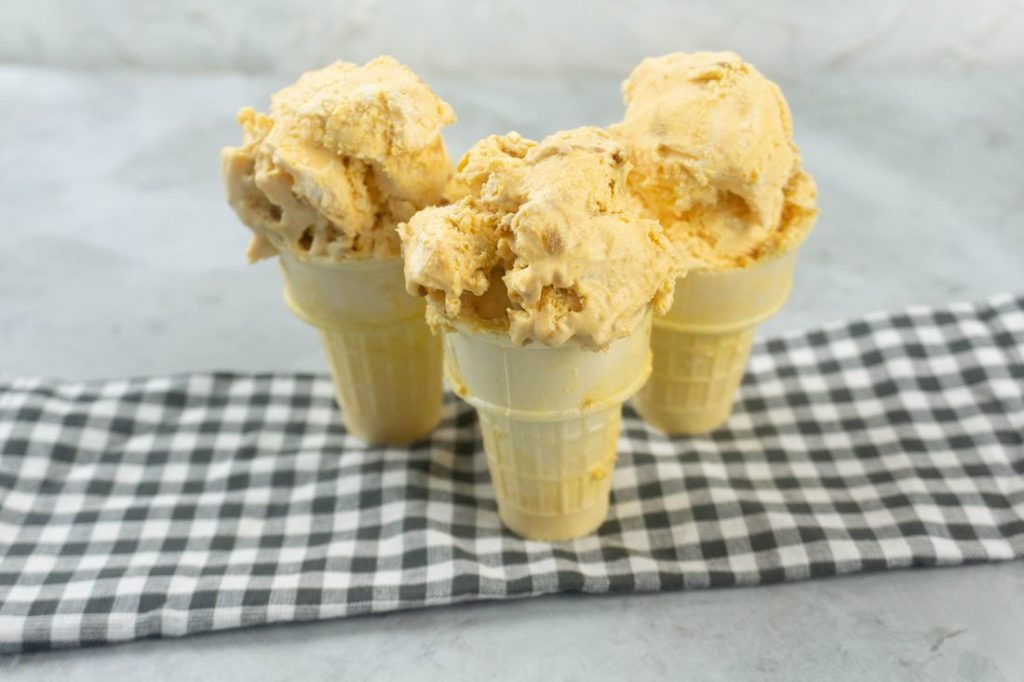 Pumpkin ginger snap ice cream in a cone on a plaid napkin with a concrete backdrop