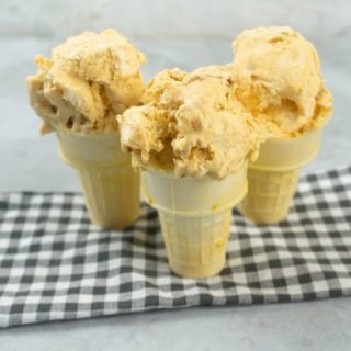 Pumpkin ginger snap ice cream in a cone on a plaid napkin with a concrete backdrop