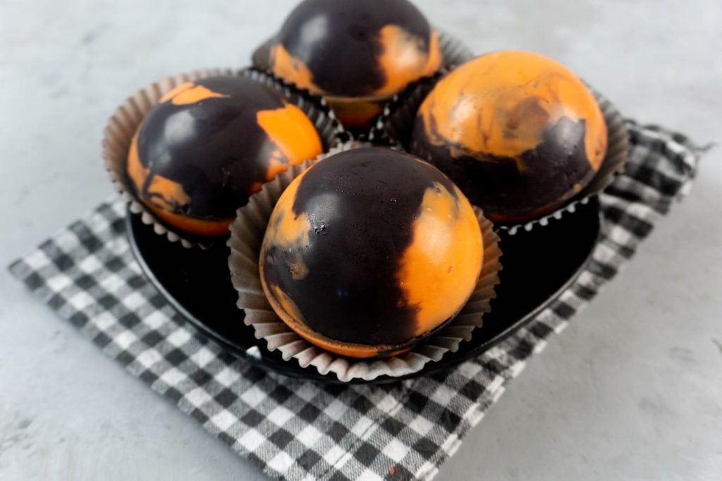 Halloween Hot Chocolate Bombs in orange and black marbled spheres on a black plate and grey plaid napkin