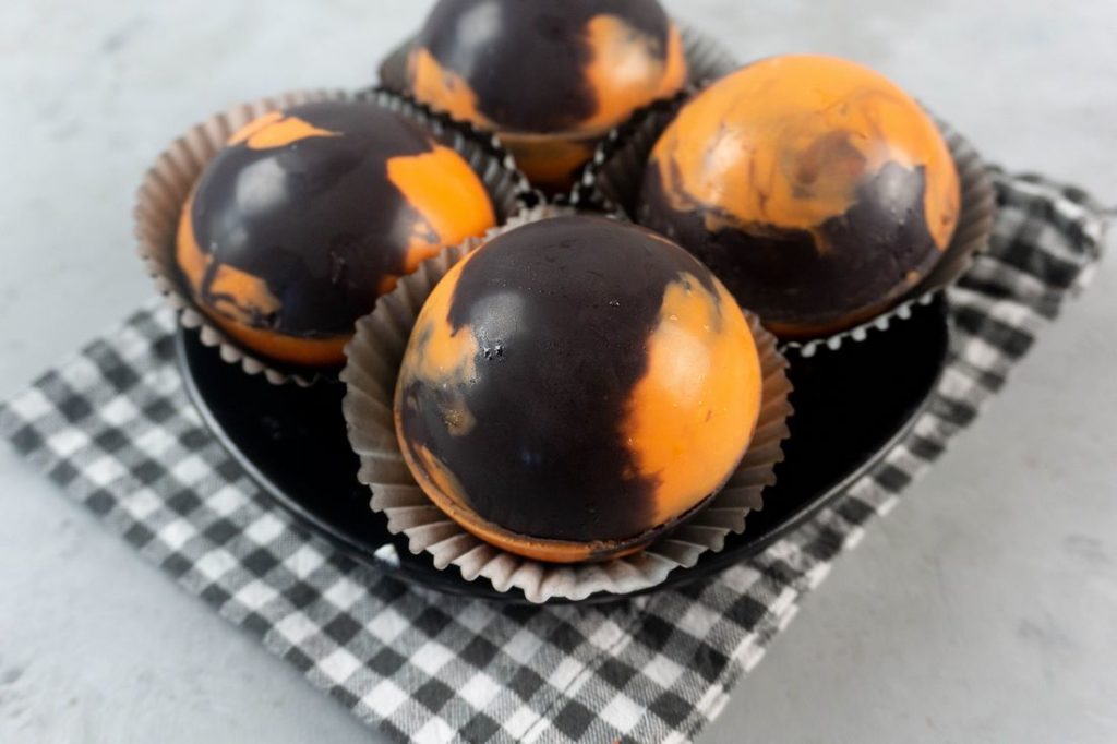 Halloween Hot Chocolate Bombs in orange and black marbled spheres on a black plate and grey plaid napkin