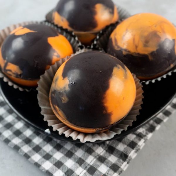 Halloween Hot Chocolate Bombs in orange and black marbled spheres on a black plate and grey plaid napkin
