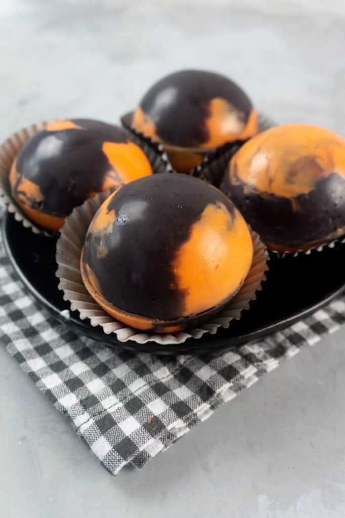 Halloween Hot Chocolate Bombs in orange and black marbled spheres on a black plate and grey plaid napkin