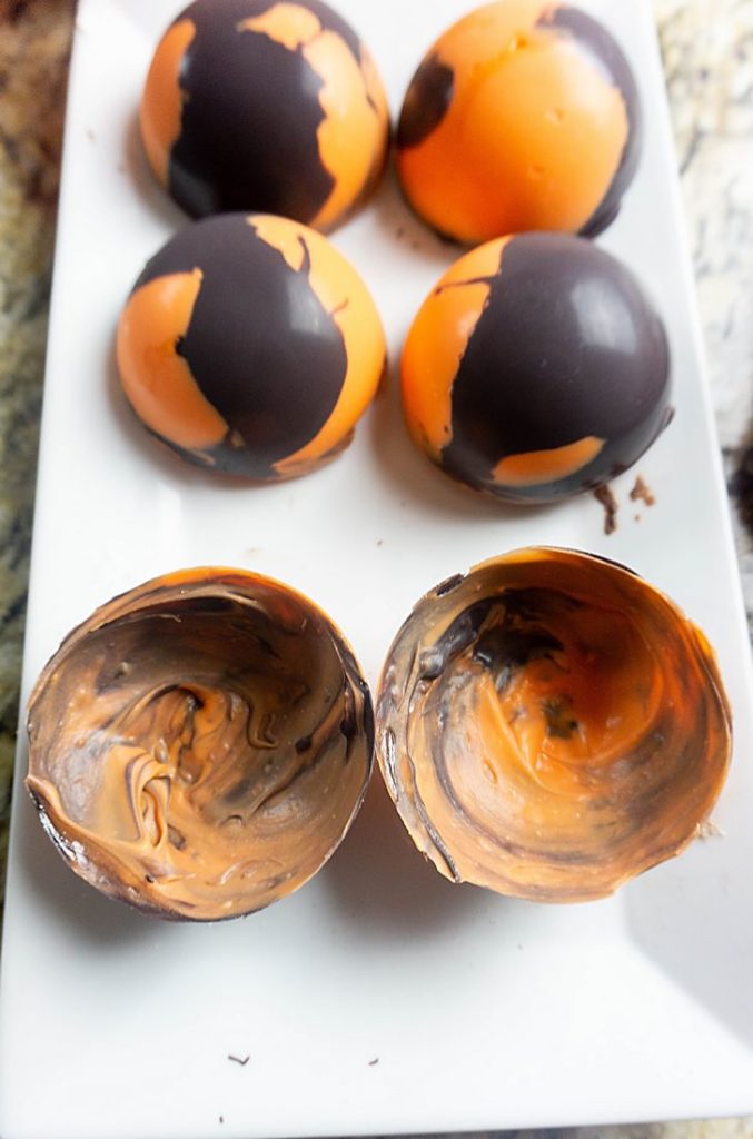 Halloween Hot Chocolate Bombs in orange and black marbled spheres on a black plate and grey plaid napkin