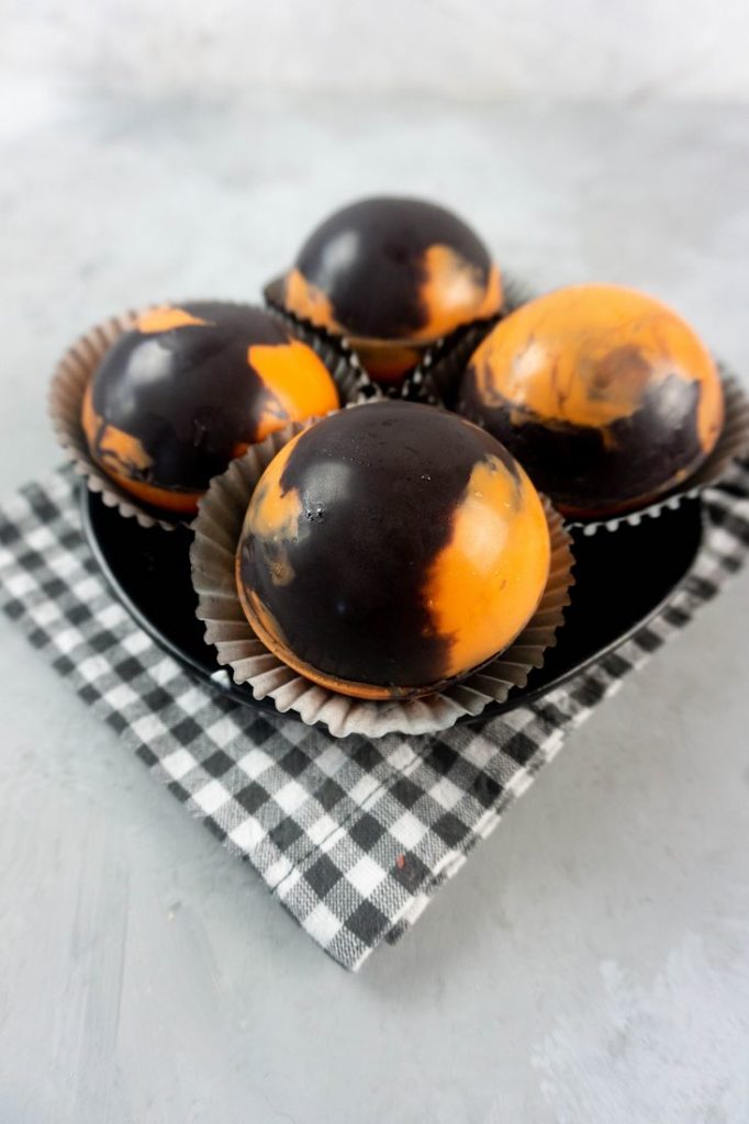 Halloween Hot Chocolate Bombs in orange and black marbled spheres on a black plate and grey plaid napkin