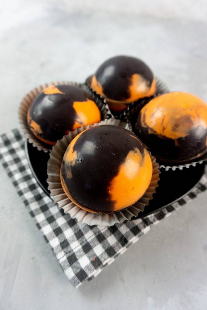 Halloween Hot Chocolate Bombs in orange and black marbled spheres on a black plate and grey plaid napkin