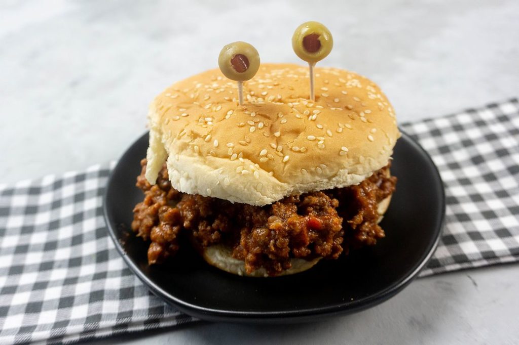 Monster sloppy joe with olive eyes and on a black plate with gray plaid napkin.