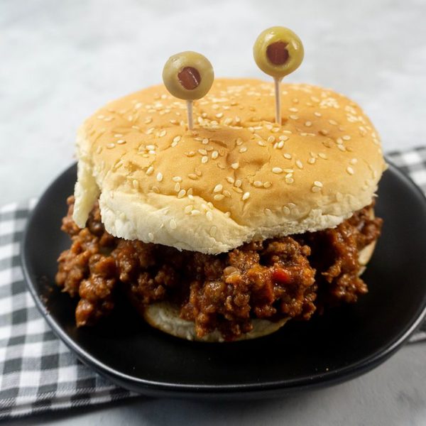 Monster sloppy joe with olive eyes and on a black plate with gray plaid napkin.