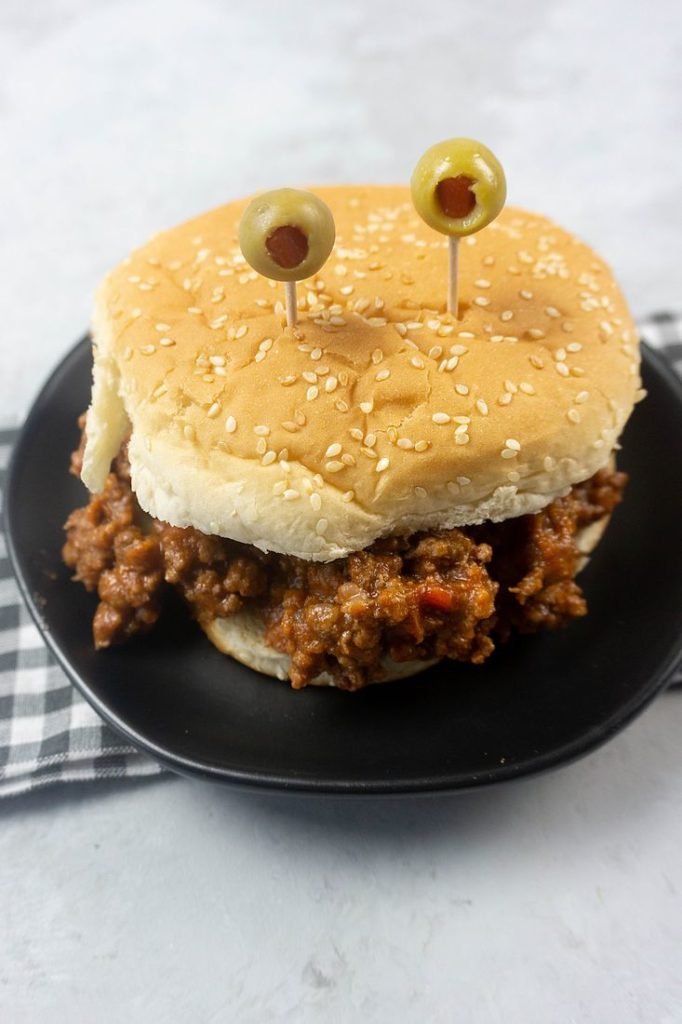 Monster sloppy joe with olive eyes and on a black plate with gray plaid napkin.