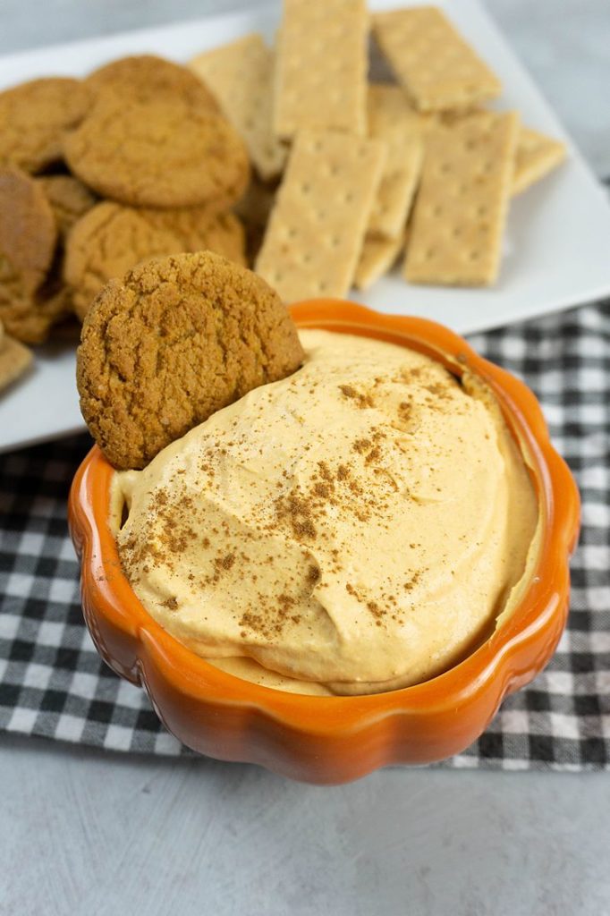 Pumpkin Cheesecake Dip in a pumpkin bowl with plaid napkin and concrete backdrop