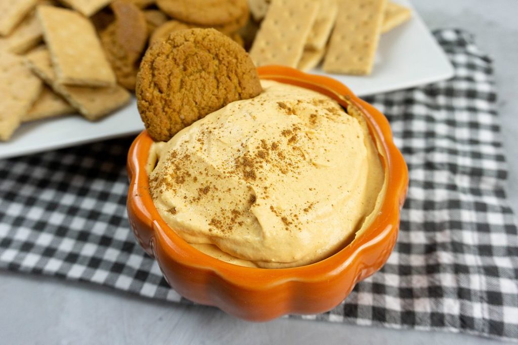 Pumpkin Cheesecake Dip in a pumpkin bowl with plaid napkin and concrete backdrop