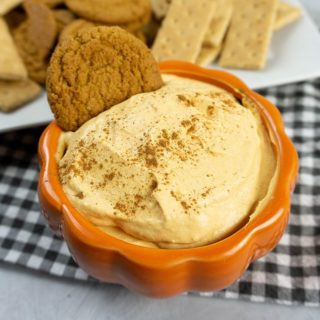 Pumpkin Cheesecake Dip in a pumpkin bowl with plaid napkin and concrete backdrop