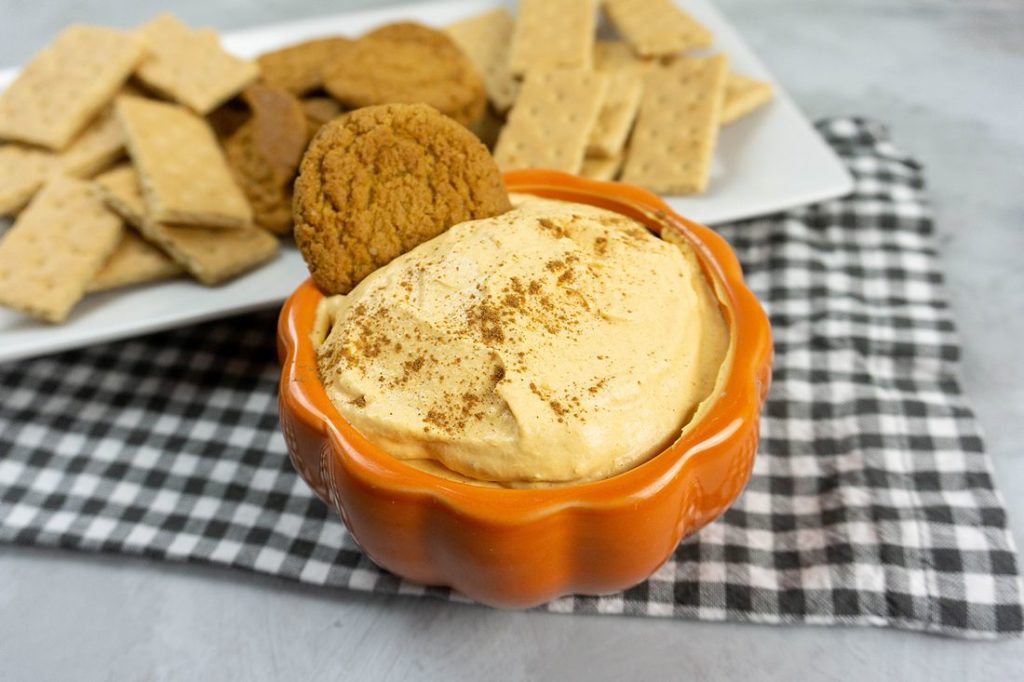 Pumpkin Cheesecake Dip in a pumpkin bowl with plaid napkin and concrete backdrop