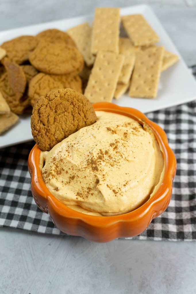 Pumpkin Cheesecake Dip in a pumpkin bowl with plaid napkin and concrete backdrop