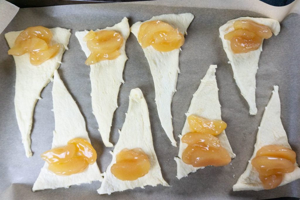 Croissant dough rolled out and filled with apple pie filling on parchment paper