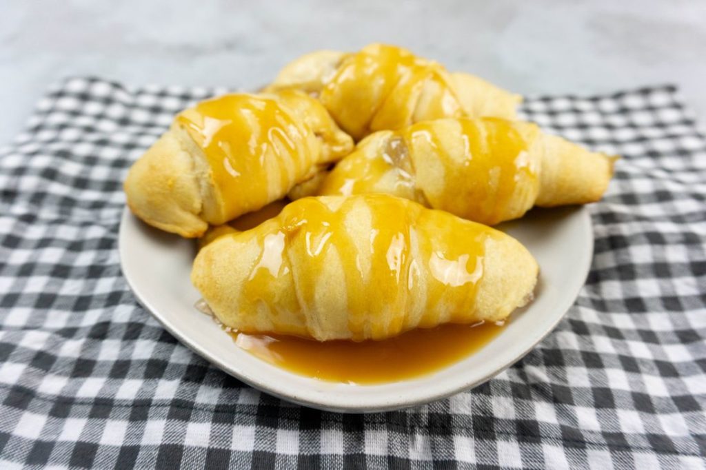 Apple Dumpling Croissants on a white plate with caramel drizzle with white and gray napkin on a concrete backdrop