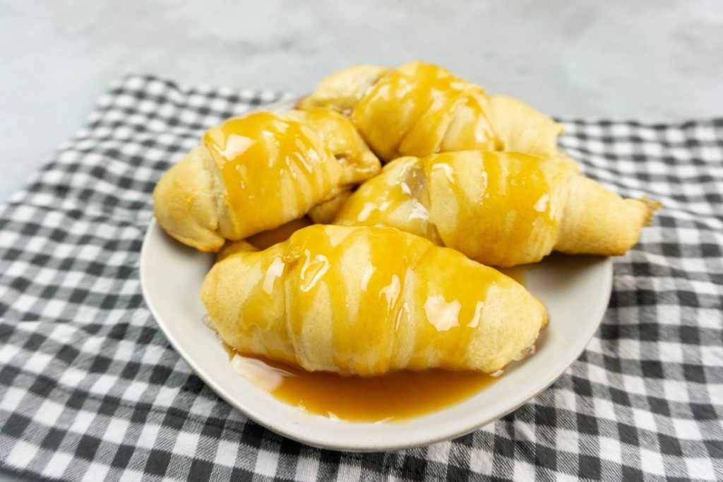 Apple Dumpling Croissants on a white plate with caramel drizzle with white and gray napkin on a concrete backdrop